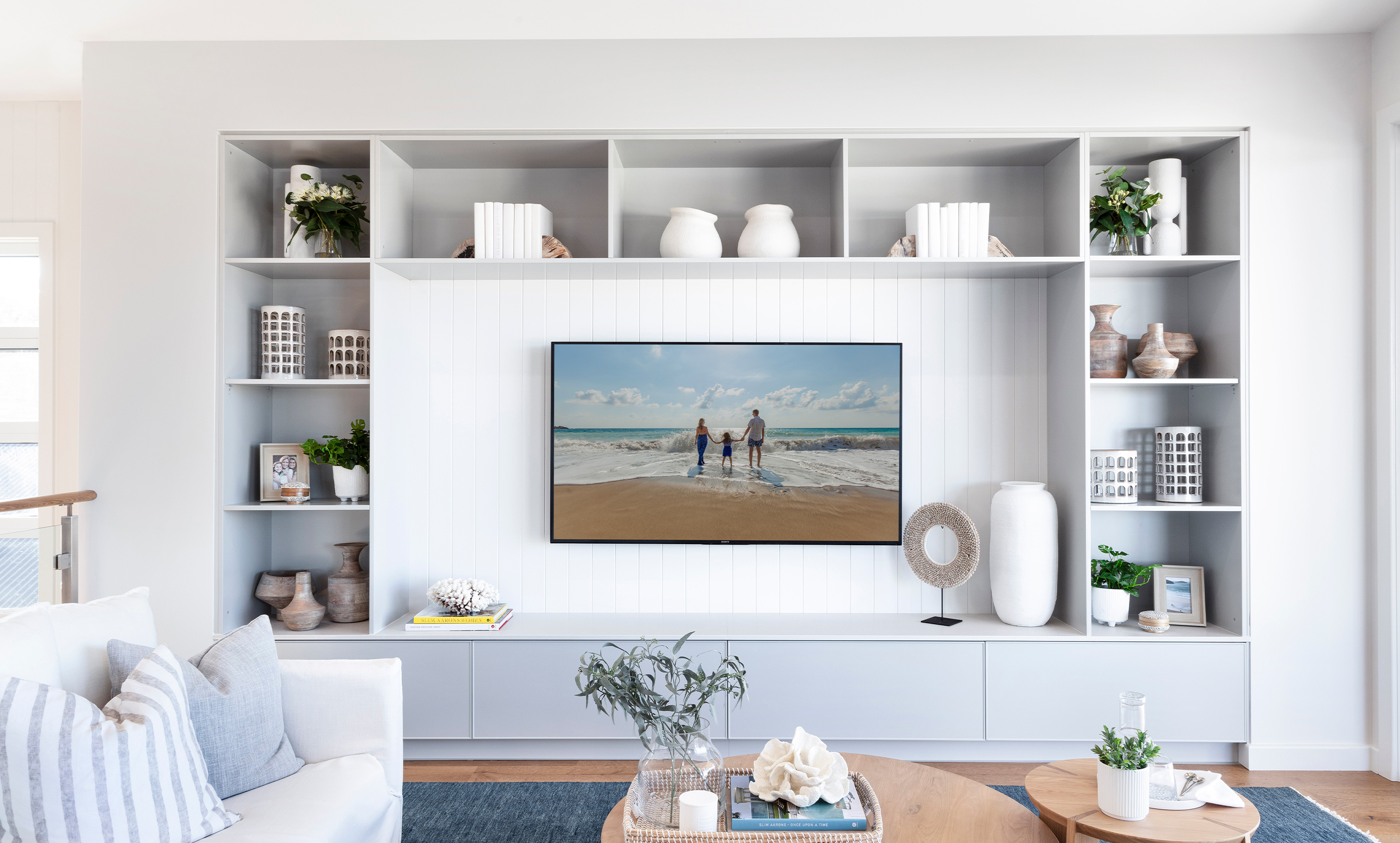 A costal styled living room and entertainment unit with predominantly white accessories and beach decor by McDonald Jones, at Sovereign Hills, Port Macquarie.