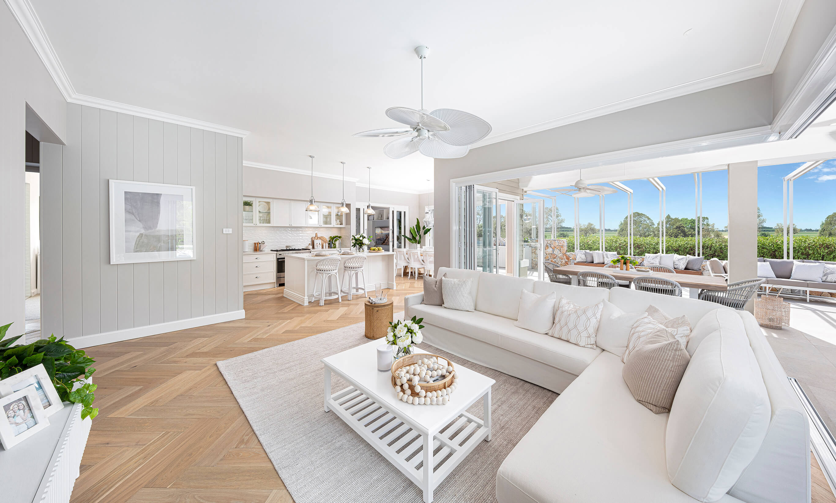 Beautiful Coastal styled living room, at Moonee Beach, featuring a Tahitian fan, plush white modular lounge suite, with open stacker glass doors and light timber flooring, built by McDonald Jones 