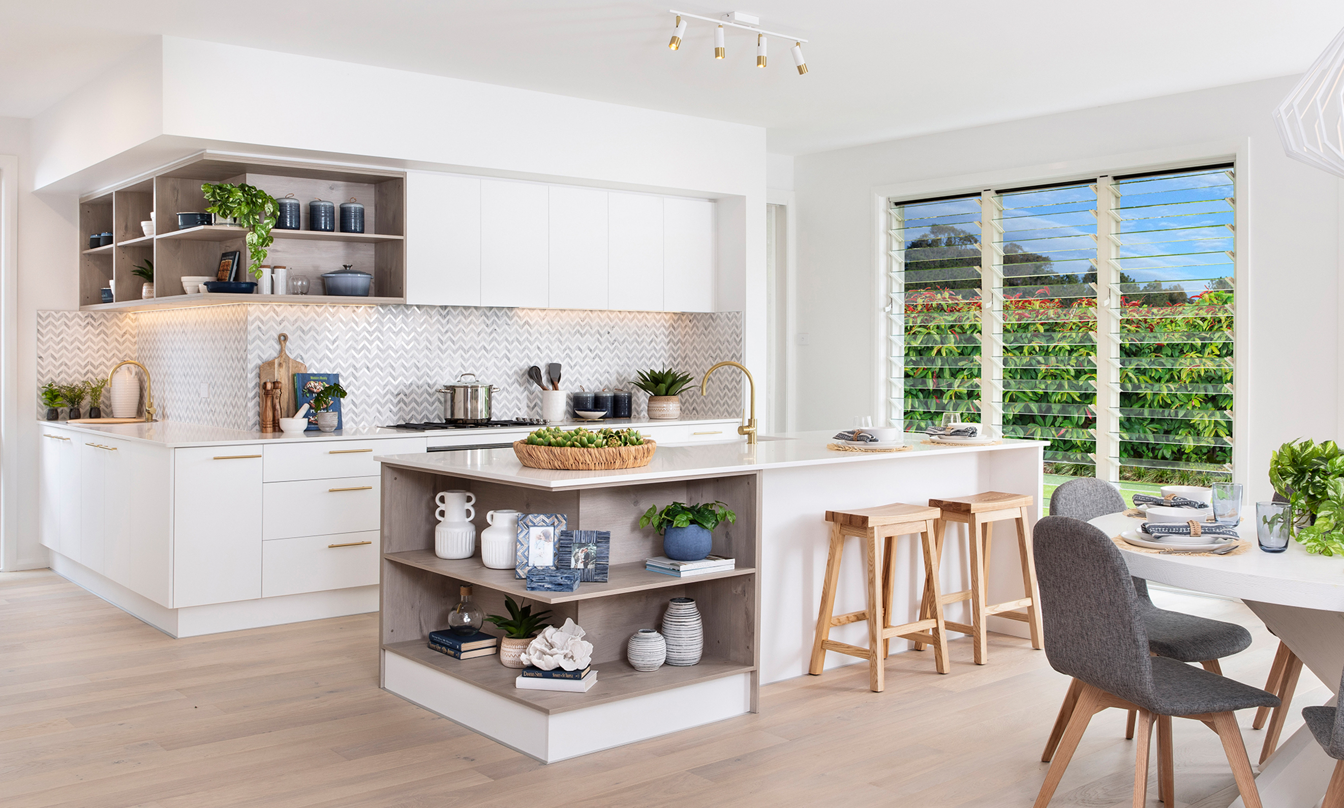 Modern Coastal styled Kitchen features glass louvers to create a light-filled and breezey space with a combination of open cabinerty and soft drift wood timbers and beautiful herringbone tiled splashback